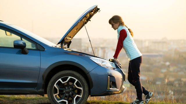 woman standing in front of broken down car not making 100k miles