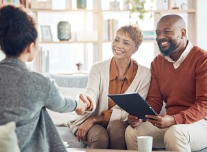 A mature couple sitting on a couch shaking a woman's hand as they prepare for a business meeting