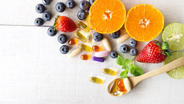 Multivitamins and supplements with fresh and healthy fruits on white wooden background.