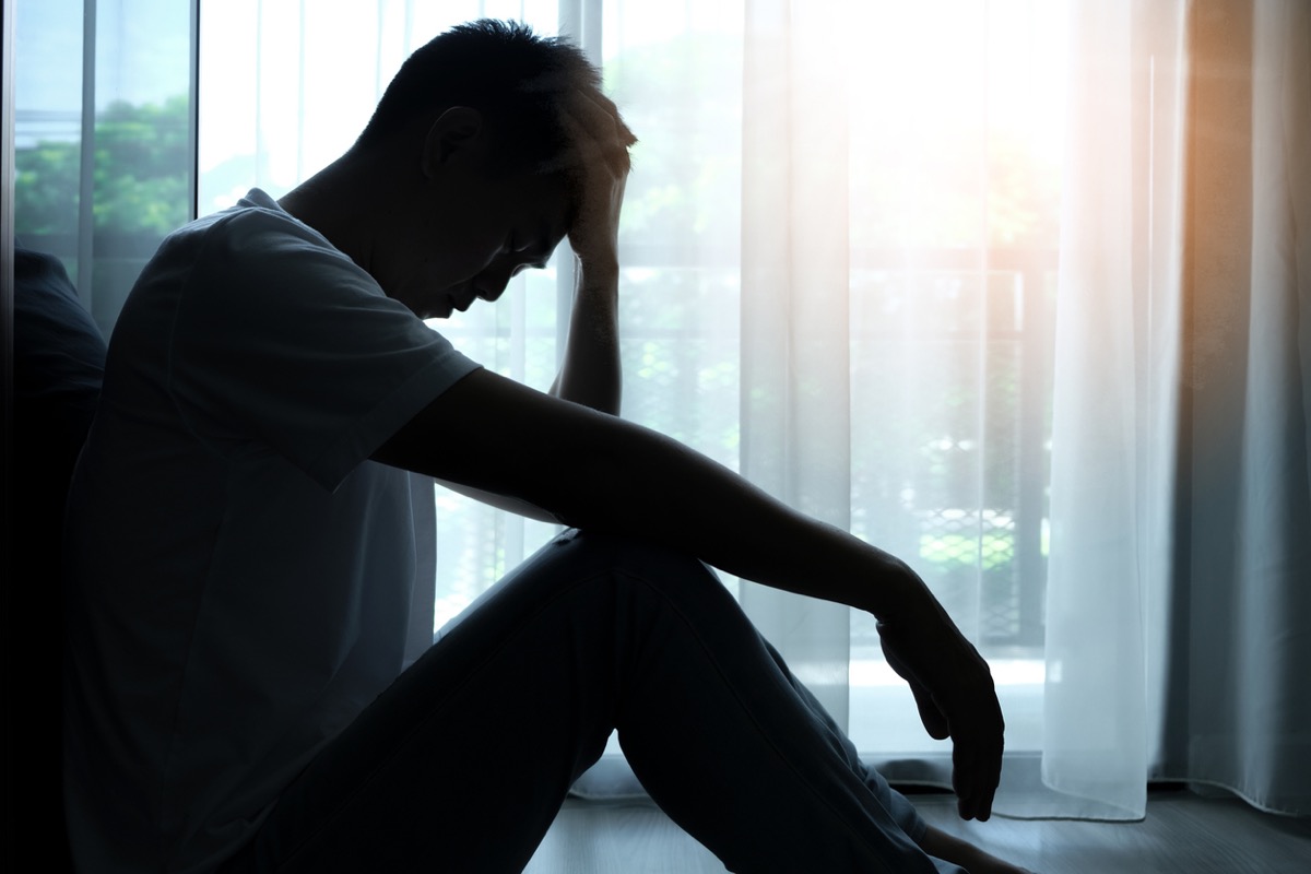 Dark image of a man sitting on the floor with his head in his hands