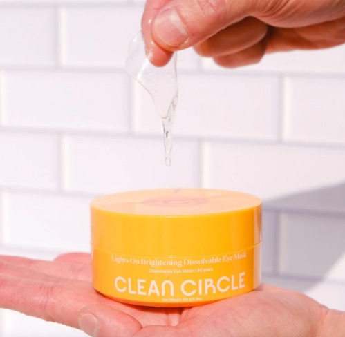 Hands holding yellow tub of Credo Beauty eye masks against a white tiled wall
