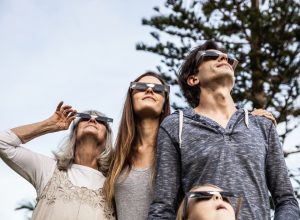 A family with four people look at a solar eclipse while wearing protective glasses