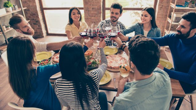 Group of friends sitting around a dinner table toasting with glasses of red wine