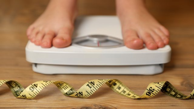 standing on scale with measuring tape in front