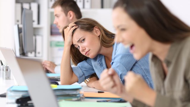 A jealous-looking young woman staring at her female coworker who's celebrating