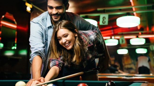 Portrait of young couple having fun playing billiard together. The man is showing the woman how to shoot pool.