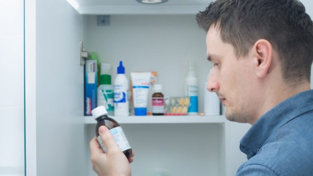 A person looking at a bottle of medicine from their medicine cabinet