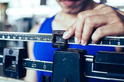 Sport man weighing himself on balance weight scale at the gym