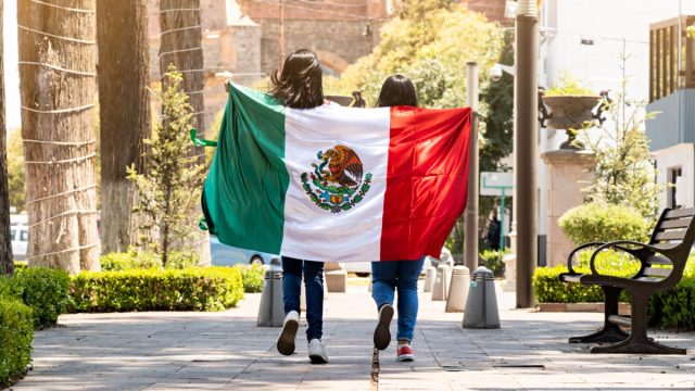 two young women running on a sidewalk with the mexican flag