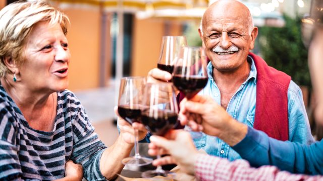 Happy senior couple having fun drinking red wine with friends at dinner party