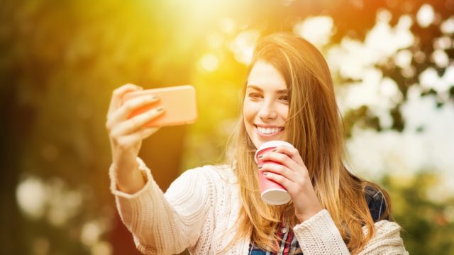 woman taking a selfie and holding a takeout coffee cup in spring time