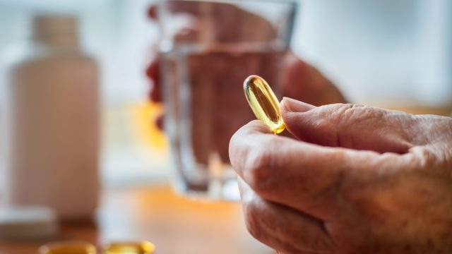 Senior woman holding omega-3 fish oil nutritional supplement and glass of water in her hands.