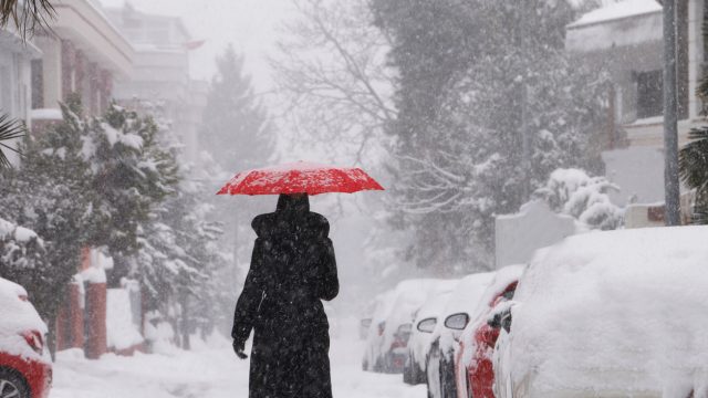 A person walking in a snowstorm in a city with a red umbrella