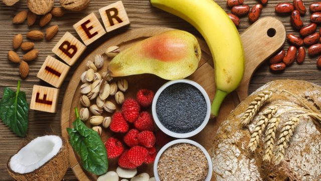 Foods rich in fiber as rye bread, wheat bran, white beans, red beans, spinach, almonds, poppy seed, pears, bananas, coconut, raspberries, pistachios, walnuts. Wooden table as background