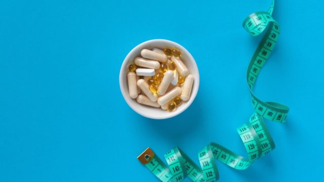 Weight Loss Pills and Measuring Tape, Diet Supplements Capsules, Obesity Lose Tablets, Color Drugs Pile, Weight Loss Pills on Blue Background with Copy Space for Text