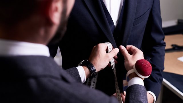Over shoulder view of bearded fashion designer fitting bespoke suit to model, close-up shot