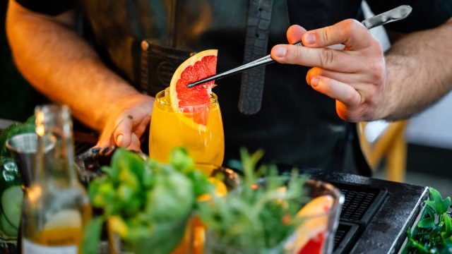 Close-up of bartender putting grapefruit in a fresh cocktail in the bar
