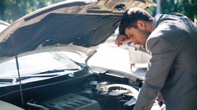Young man looking under the hood of breakdown car