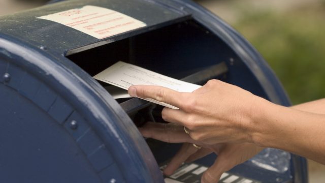 A close up of someone putting envelopes into a blue mailbox