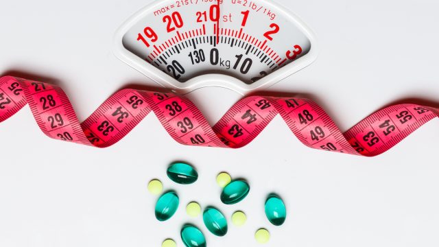 Closeup of a white scale with a red tape measurer and blue/green supplements