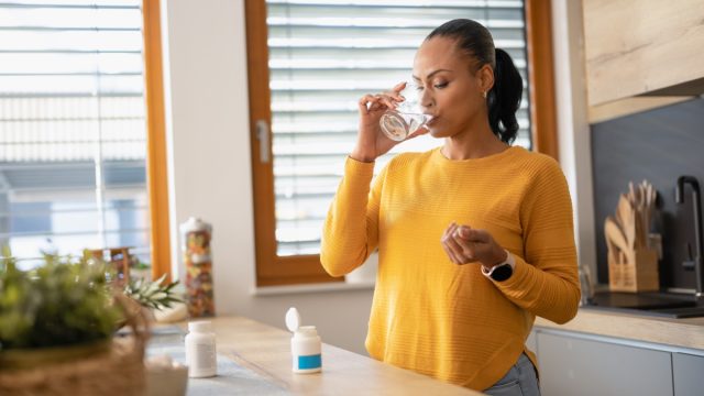 Young woman taking medicine, vitamin with water at home. Modern lifestyle and healthcare concept.
