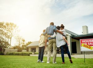 A family standing in front of a house with a "sold" sign in the yard