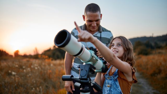 A father and his daughter looking at the sky using a telescope