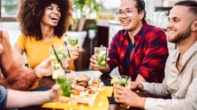 Young friends raising their cocktails to cheers at a dinner party