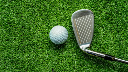Golf club and golf ball close up in grass field with sunset.