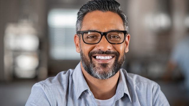 Smiling mature indian man wearing spectacles and looking at camera. Portrait of middle eastern confident businessman at office. Portrait of successful mid entrepreneur feeling satisfied and working from home.