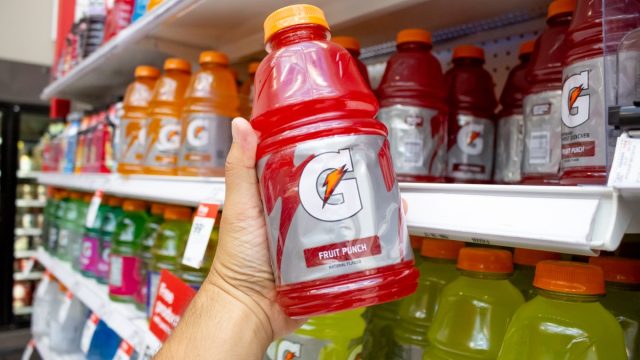 A view of a hand holding a bottle of Gatorade, on display at the grocery store.
