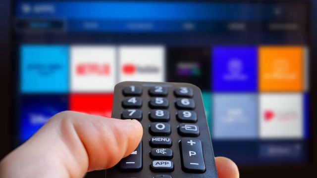 A close up of someone holding a remote and pointing it at a TV with streaming services on it