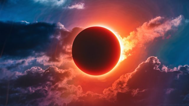 A close up of the sun covered up by the moon during a solar eclipse with clouds around it