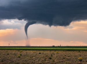 A tornado touching down in a field with a dark cloud above it