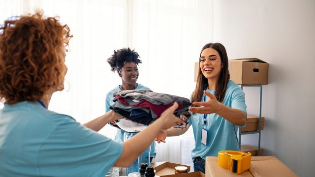 Three female volunteers wearing light blue t-shirts collecting donated clothing