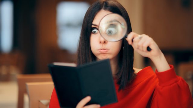 Woman in a red sweater looking at a restaurant bill with a magnifying glass