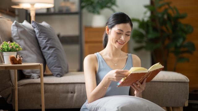 Young woman sitting on the floor reading a book in her reading nook