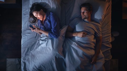 Couple laying in bed while woman texts other people