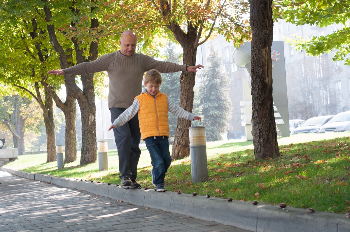 Grandfather and his grandson playing in the park, doing a balance walk