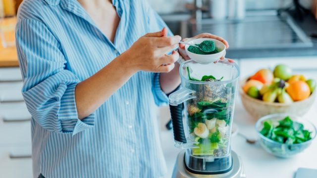 Woman adding spirulina green powder to green smoothie