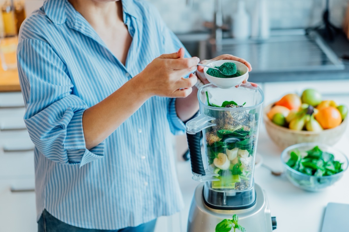 Woman adding spirulina green powder to green smoothie