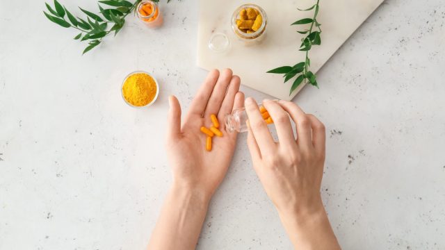 Female hands with turmeric pills, powder and roots on light background