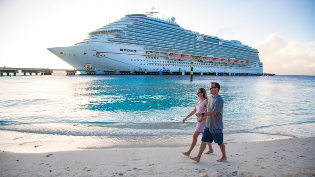 Middle aged couple enjoying a Caribbean Cruise vacation together. Candid photo of a couple holding hands and walking together on a beach with a Cruise ship in the background