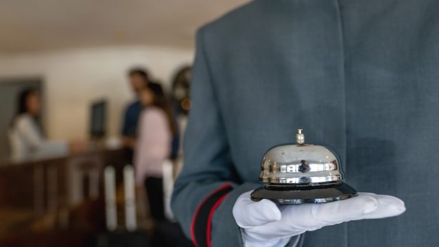 A close up of a bellhop's hand holding a bell in a hotel lobby