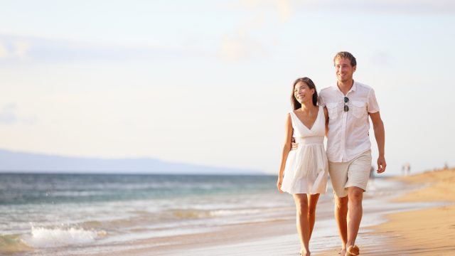 couple wearing white clothes walking arm-in-arm on the beach