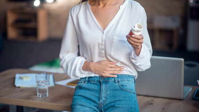 Feeling pain. Pleasant young woman putting hand on her stomach while feeling pain in it