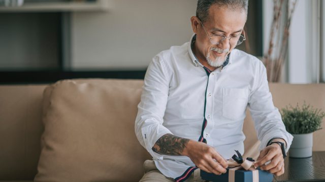 A man opening up a present while sitting on a couch