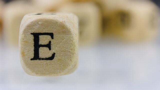 The letter E on a wooden cube with other dice letters in the background