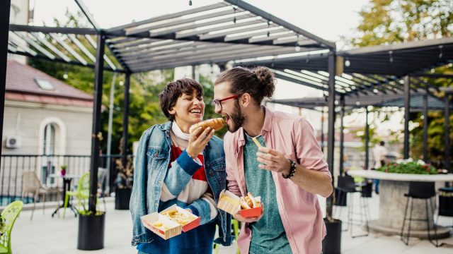 Young couple is eating hot dog outdoors and having fun