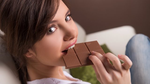 Woman eating chocolate. Beautiful young woman sitting on the coach and eating chocolate